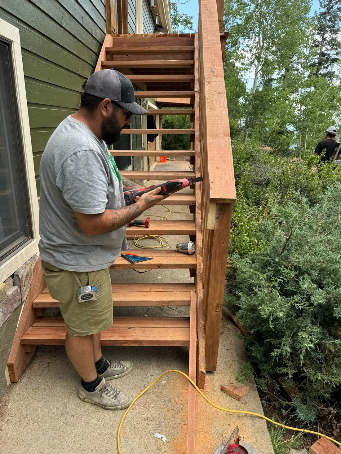 Handyman with a drill finishing a new wooden staircase beside a house