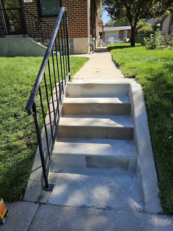 Concrete front steps with a new black metal handrail