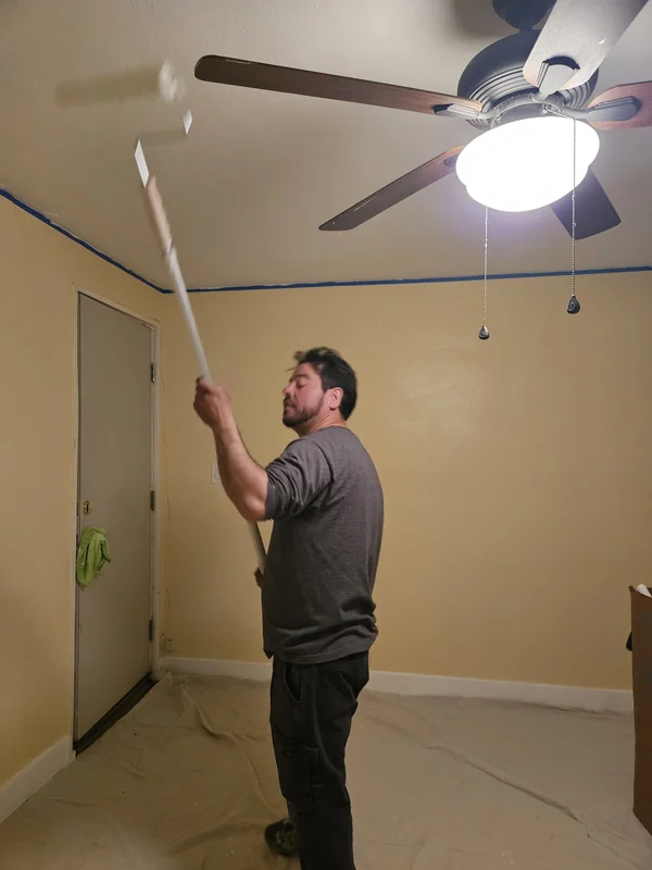 Painter using an extension roller on a yellow bedroom wall