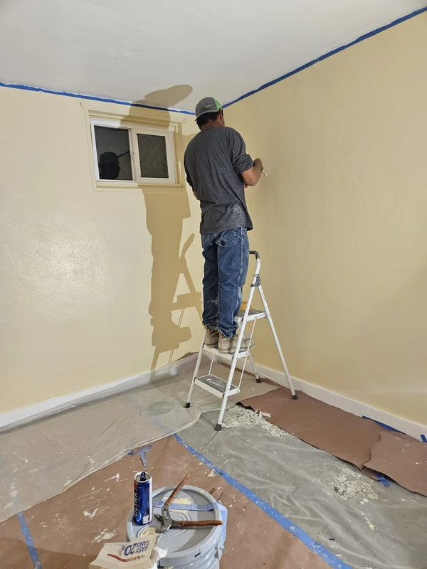 Worker patching a wall beside a window before painting